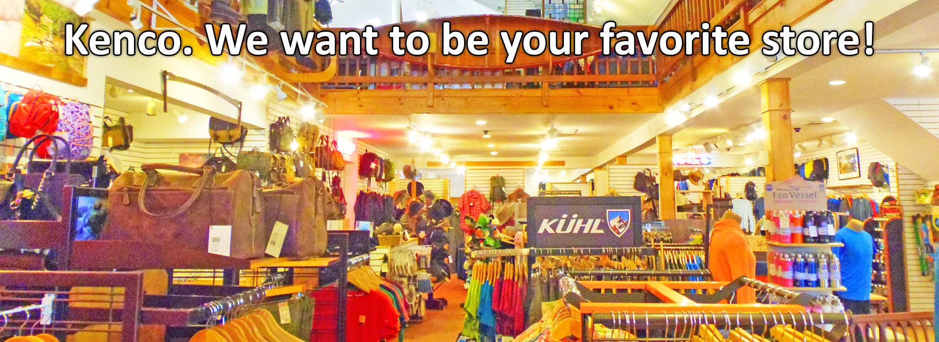 Kenco. We want to be your favorite store! Image description: The Kenco Outfitters main floor showroom. There are racks of clothing, water bottls, hats, backpacks, leather duffel bags, and waxed canvas bags visible. The upper floor of the store is slightly visible at the top of the image with a canoe mounted to the railing above straight ahead, and chest waders hanging from the railing to the left. The store is well lit and has white slatwalls with natural wood accents